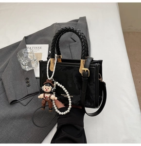 Detail of black mini bag with woven handle, pearl chain decoration and cartoon charm