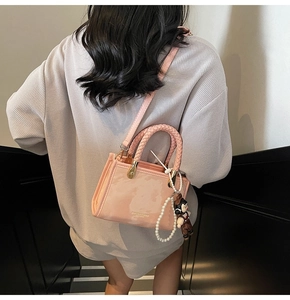 Pink crossbody bag featuring a woven handle, pearl charm and decorative doll detail