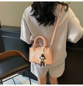 Detail of pink jelly crossbody bag with woven handle and a pearl charm on a model