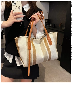 Detail of striped canvas tote bag with brown leather handles and decorative straps