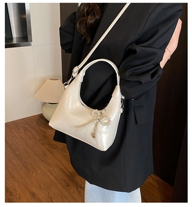 Detail of cream hobo bag featuring pearl bow charm and glossy leather texture