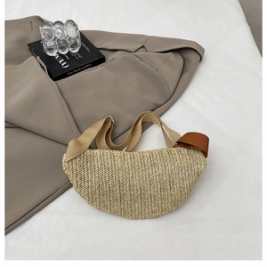 Detail of woven straw crescent crossbody bag with textile strap on styled background