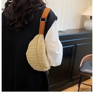 Close-up of a woven straw moon bag with brown fabric strap and metal zipper detail