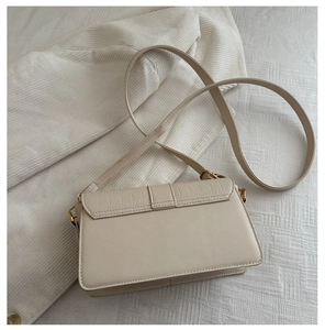 Detail view of cream shoulder bag featuring crocodile pattern flap and gold metal buckle