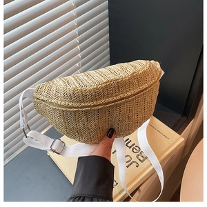 Detail of hand-held straw woven crescent belt bag with white adjustable strap and silver rings