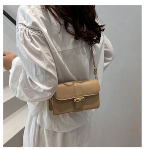 Sac à bandoulière beige à motif crocodile avec fermoir bambou doré porté par un mannequin