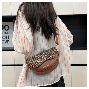 Detail of a brown saddle bag featuring a leopard print flap and wide textile strap