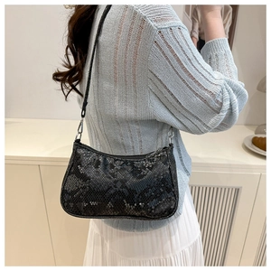 Détail du sac baguette noir texture serpent avec boucles argentées porté par un mannequin