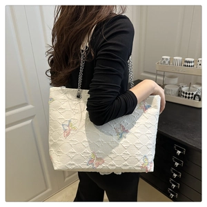 Detail of white quilted tote bag featuring butterfly embroidery and silver chain strap