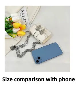 Mini white crossbody bag with silver bow detail shown next to a smartphone for scale