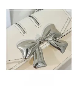 Detailed close-up of cream leather mini bag with decorative silver metal bow and stitching