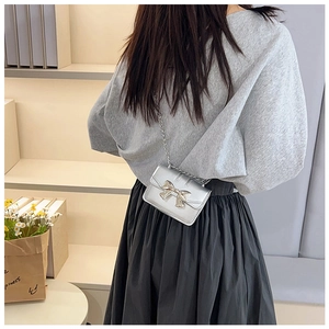 Silver metallic mini crossbody bag with gold bow detail worn by a girl on shoulder