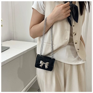 Kids black retro mini chain bag with silver bow detail shown on model in home setting
