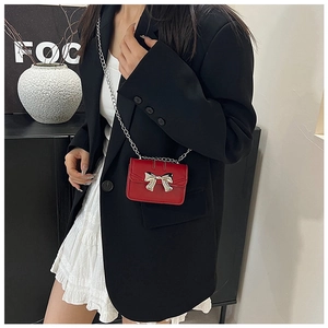 Close-up of red mini crossbody bag with silver bow buckle on black blazer jacket