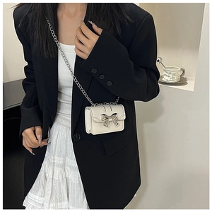 Mini white crossbody bag featuring silver bow buckle and metal chain strap on model