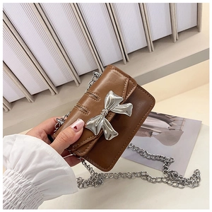 Close-up of brown mini leather crossbody bag with silver metal bow and chain strap