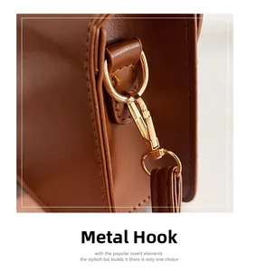 Detailed macro view of golden metal lobster clasp and D-ring on brown leather bag