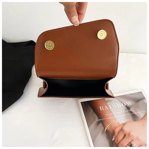 Close-up of brown leather crossbody bag featuring dual golden magnetic snap closures