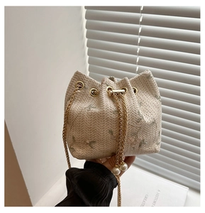Detail of woven bucket bag featuring floral embroidery and elegant pearl chain drawstrings