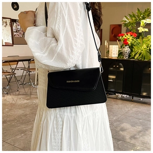 Detail of black flap crossbody bag with gold text print and textured leather panel