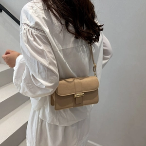 Minimalist beige leather crossbody bag with elegant gold bamboo buckle shown on model