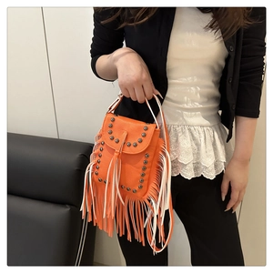 Detalle de bolso bandolera naranja con flecos largos y remaches metálicos estilo bohemio