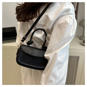 Close-up of black retro saddle bag featuring a knotted handle and adjustable strap