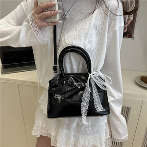 Sac en cuir verni noir avec nœud en dentelle blanche porté à l'épaule par le modèle