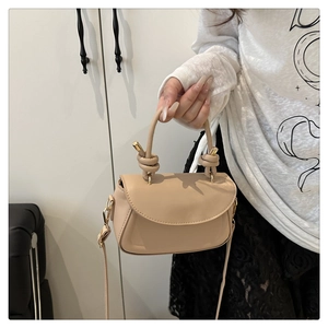 Detailed view of beige saddle bag featuring a unique twisted leather handle and gold hardware