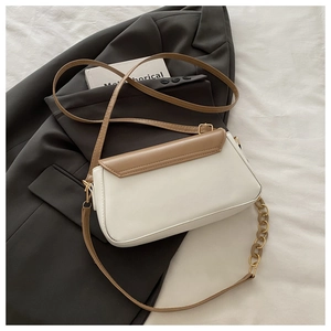 Detalle del bolso bandolera crema y marrón con cadena de resina sobre blazer gris