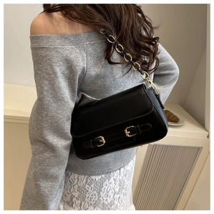 Detalle del bolso bandolera negro con correas decorativas y cadena dorada sobre el hombro