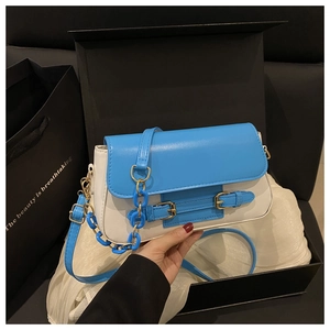 Detalle del bolso de cuero en contraste azul y blanco con cadena y hebillas doradas