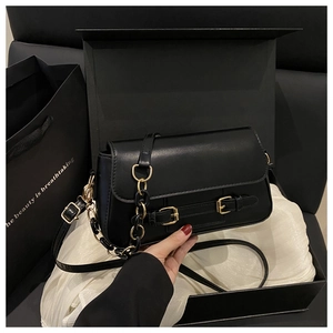 Detalle de bolso bandolera negro con herrajes dorados en caja de regalo de lujo