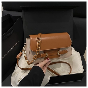 Detalle de un bolso bandolera marrón y beige con correas decorativas y asa de cadena gruesa
