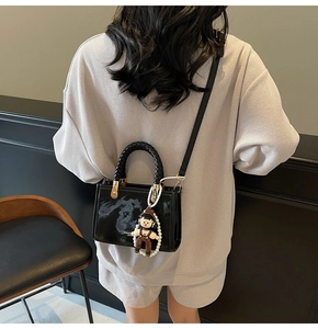 Detail of black glossy handbag with pearl chain and doll charm shown on model