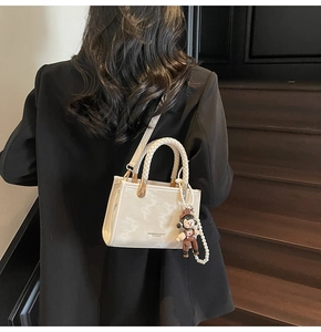 Detail of off-white marble pattern handbag with pearl bear charm on a female model