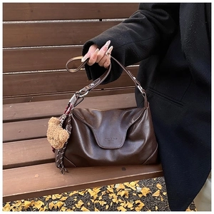 Dark coffee brown shoulder tote bag with plush bear charm in an autumn outdoor setting