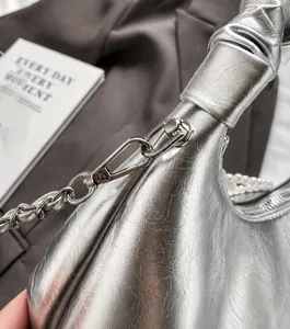 Detail of silver pleated leather handbag with knot handle, pearl strap and metal chain