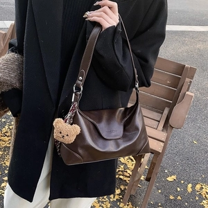 Dark brown leather tote bag with bear charm shown on model in an outdoor autumn setting