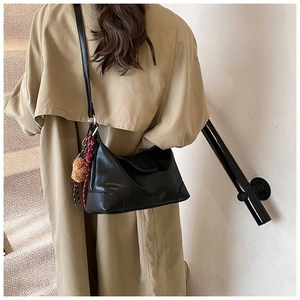 Detail of black leather hobo bag with teddy bear charm and striped scarf on soft stairs