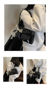 Detail of black patent leather bag with a white lace bow and dual top handles