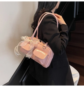 Pink patent leather shoulder bag with white lace bows and pockets shown on a black blazer