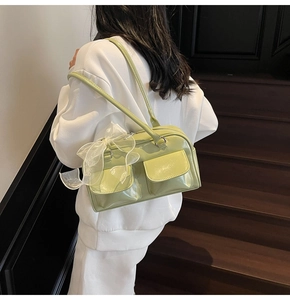 Detail view of avocado green glossy leather shoulder bag with side bow on a model