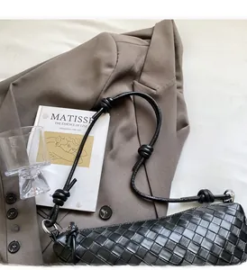 Detail of black woven leather croissant bag with knotted strap on a brown blazer