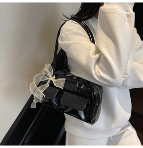 Detail of glossy black leather shoulder bag with white organza bow and front pockets