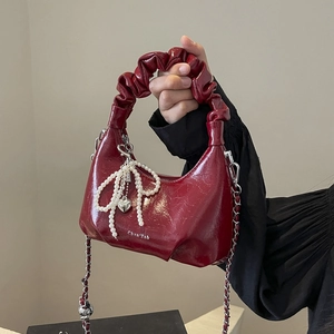 Glossy burgundy half-moon handbag with ruched handle and pearl bow charm detail