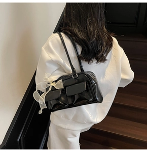 Detail of black patent leather shoulder bag with elegant white organza bow accessory