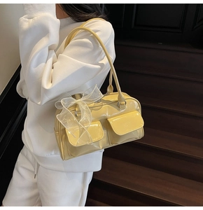 Detail of yellow patent leather handbag featuring front pockets and a white mesh bow