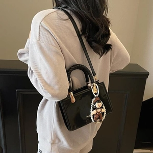 Glossy black patent leather handbag with woven handle and cute pendant charm accessory