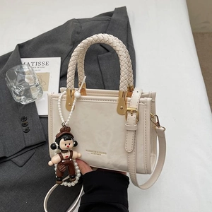 Chic beige square handbag with woven handle and charm on grey blazer background